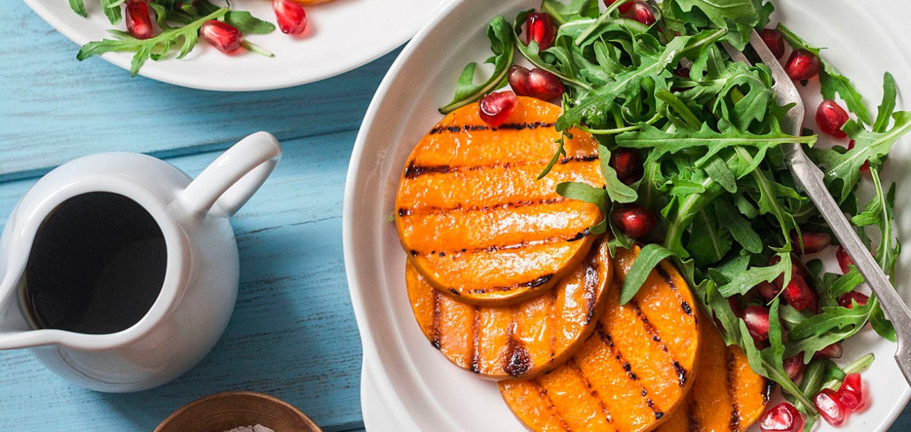90427128 - grilled butternut squash, arugula and pomegranate salad on a blue wooden table, top view. clean, organic, seasonal, vegetarian food concept