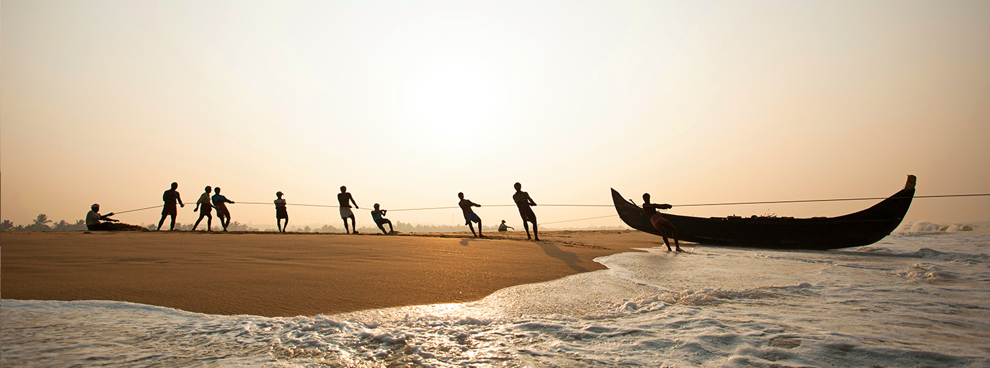 Ten fisherman use ropes to pull a small boat out of the water and onto a beach.