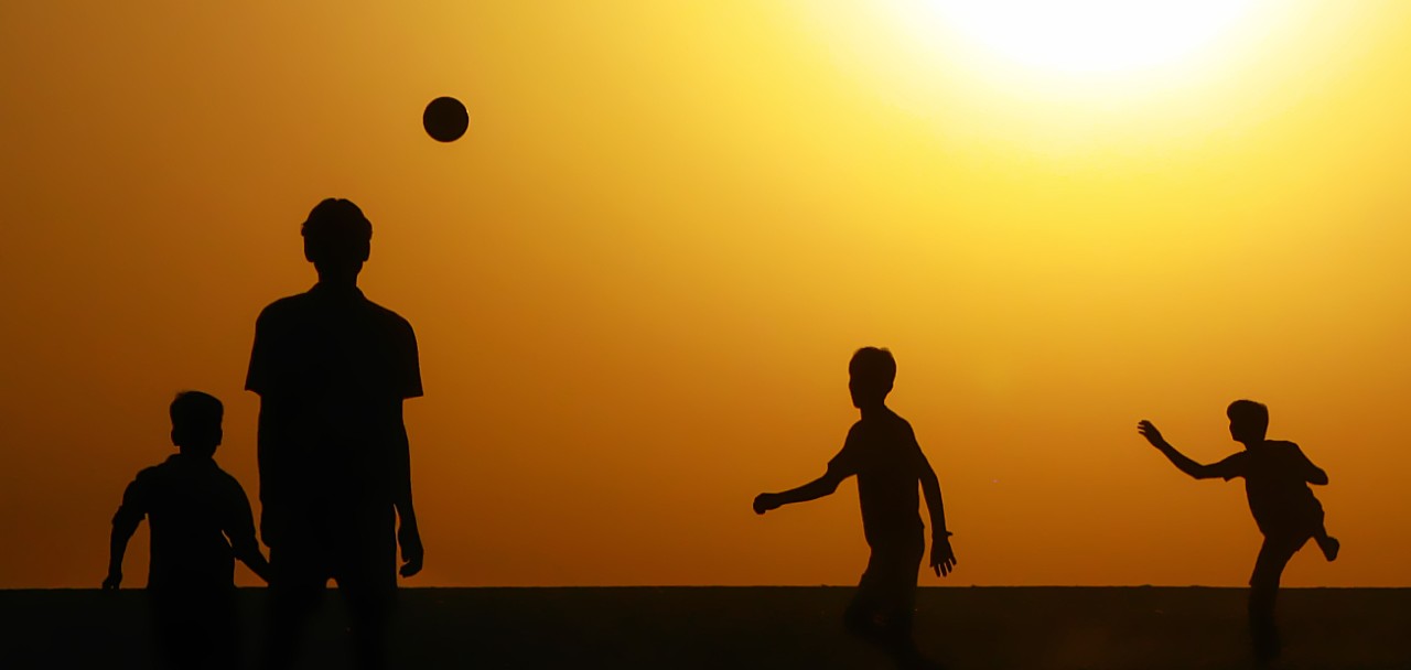 Silhouette of boys playing football against a warm sunrise sky.