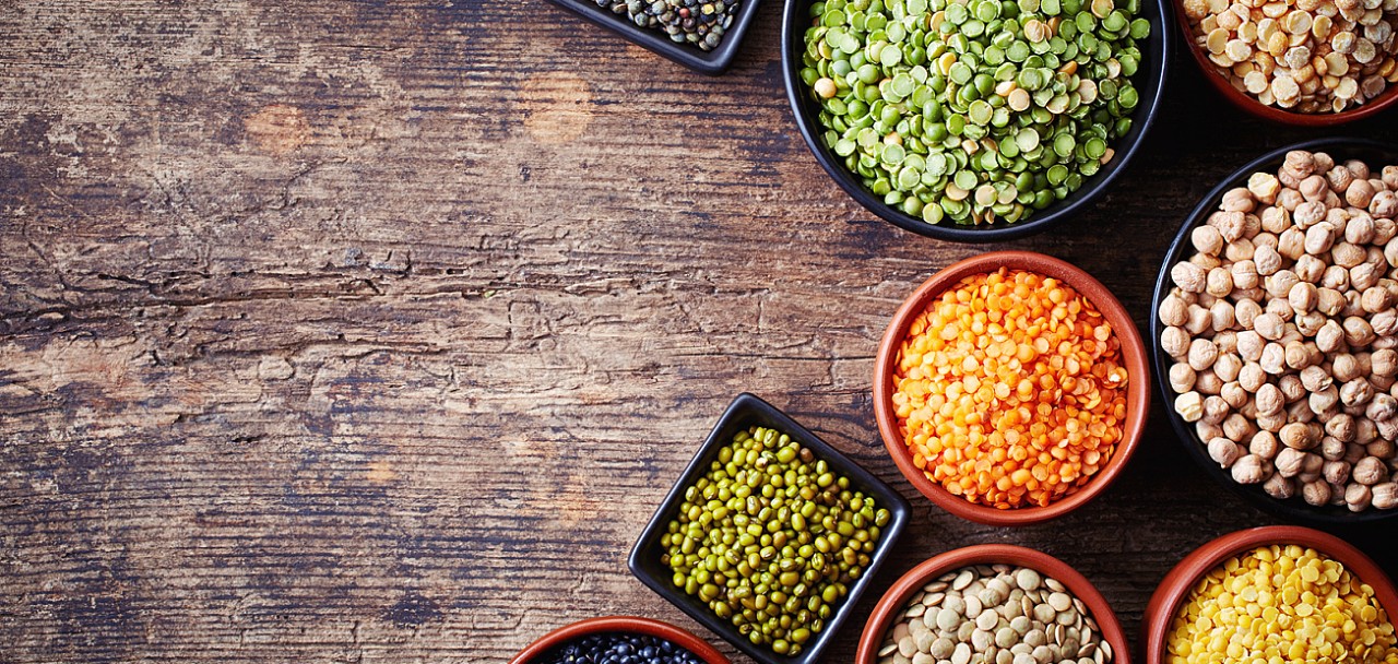 Bowls of various legumes (chickpeas green peas red lentils canadian lentils indian lentils black lentils green lentils; yellow peas green mung beans) on wooden background