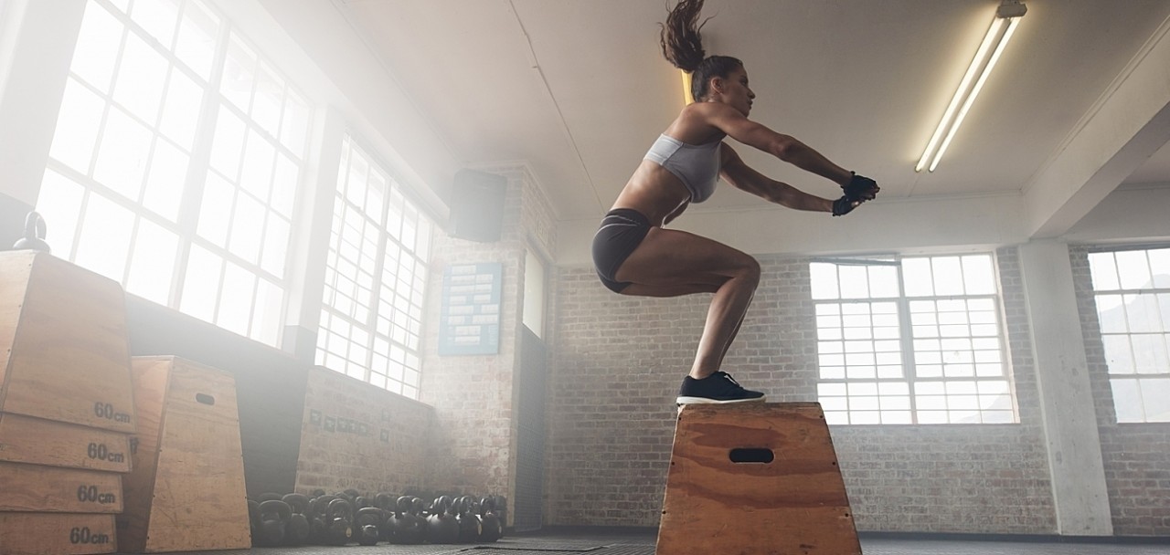 Side view image of fit young woman doing a box jump exercise. Muscular woman doing a box squat at the cross fit gym