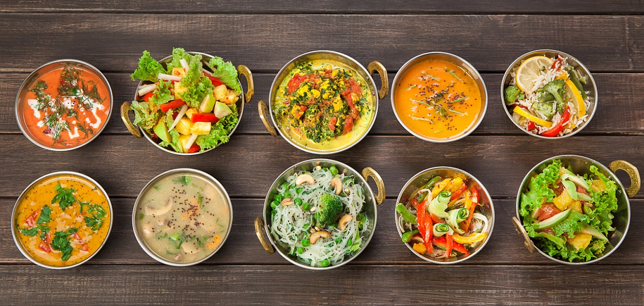 Vegan or vegetarian restaurant dishes top view, hot spicy indian soups, rice and salads in copper bowls. Traditional indian cuisine meal assortment on wood background. Healthy eastern local food