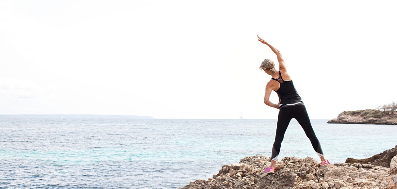 Panoramic rear view of a healthy mature woman figure stretching and exercising on a rock platform by blue sea in a nature coastal destination, outdoors. Fitness and body care senior lifestyle.; Shutterstock ID 471950543; PO: 123