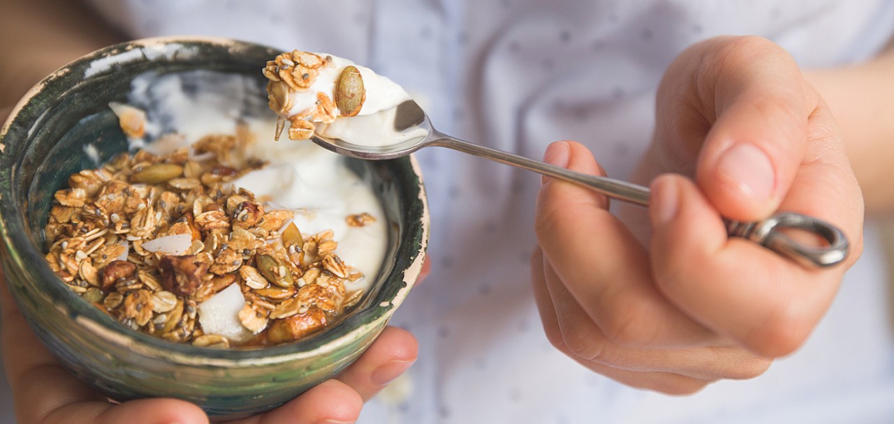 Young woman with muesli bowl. Girl eating breakfast cereals with nuts pumpkin seeds oats and yogurt in bowl. Girl holding homemade granola. Healthy snack or breakfast in the morning.