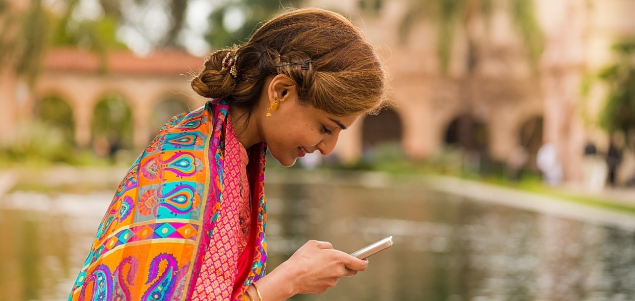 Woman in colorful clothing, sitting in a park, texting; technology, smart phone, cell phone; Shutterstock ID 417324376; PO: 123